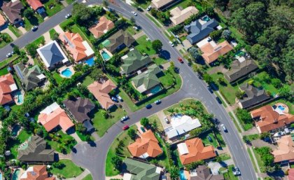 An aerial photo of a typical Australian suburb, showing roads, house rooftops, backyards and swimming pools. 